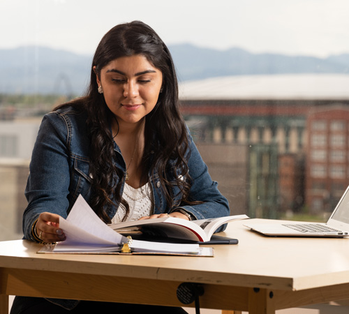 CU Denver student looking at notes while sitting at table with laptop