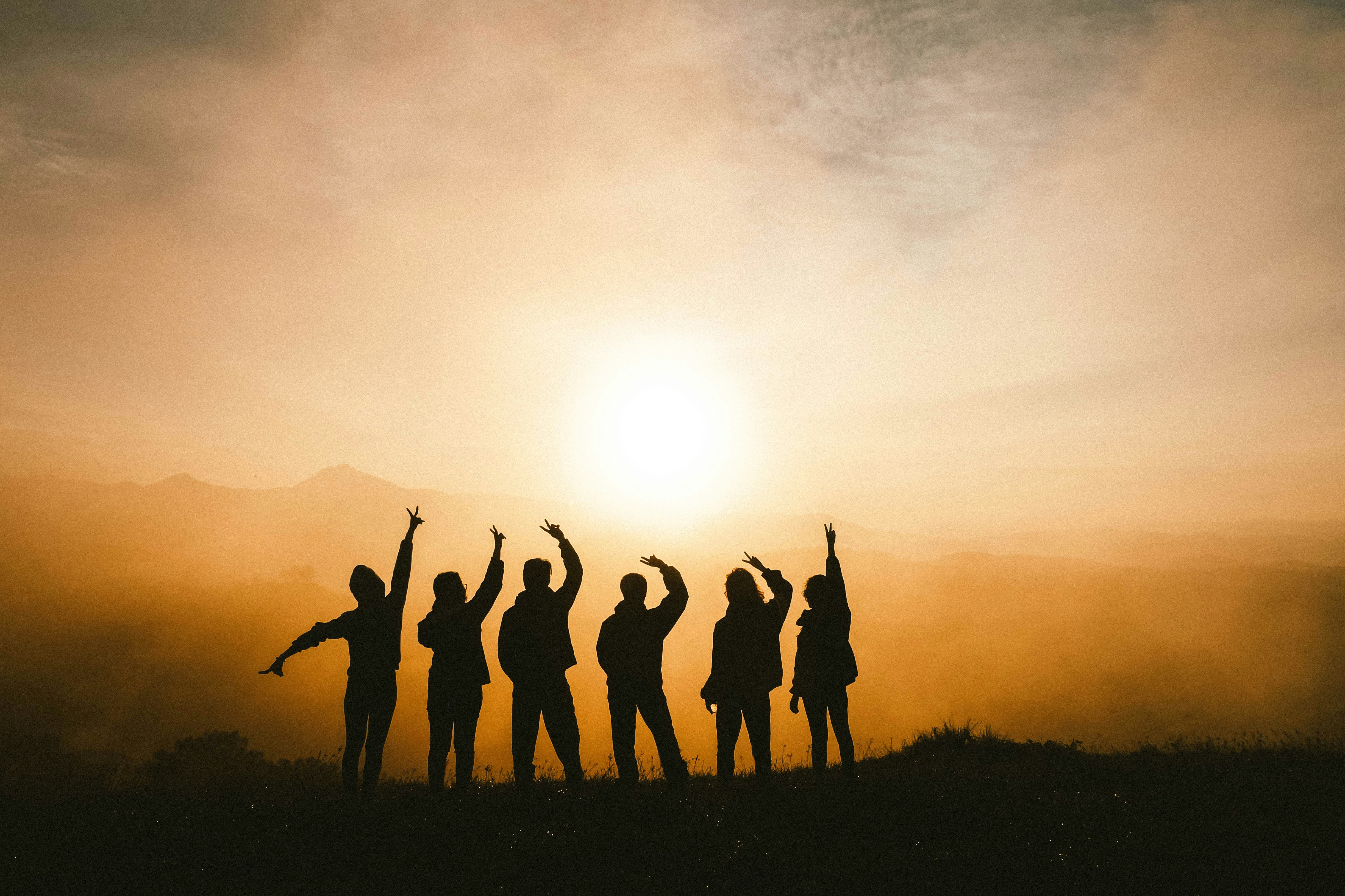 group of people reaching toward the sun