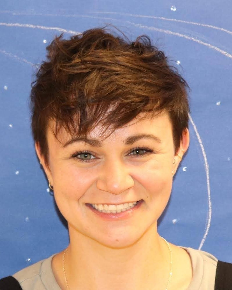Lindsay has short brown hair, light skin, and is pictured in front of a blue background.