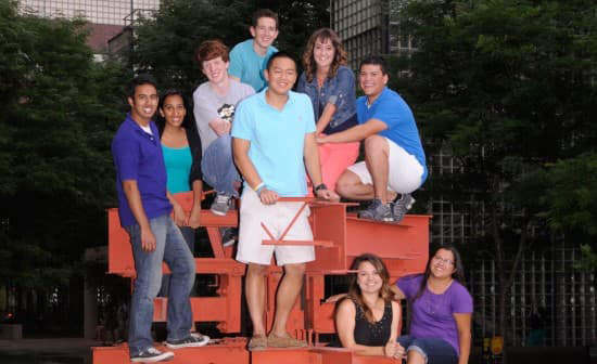 Scott Cao and other students from the class of 2017 sit smiling on a campus sculpture.