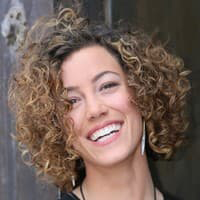 Zoe Dohnal portrait with brown, short curly hair and smiling with her teeth.
