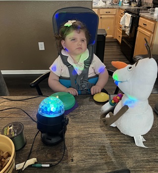 young child sits with postural seat, facing two options of switch activated toys - a light up disco ball and a talking Olaf