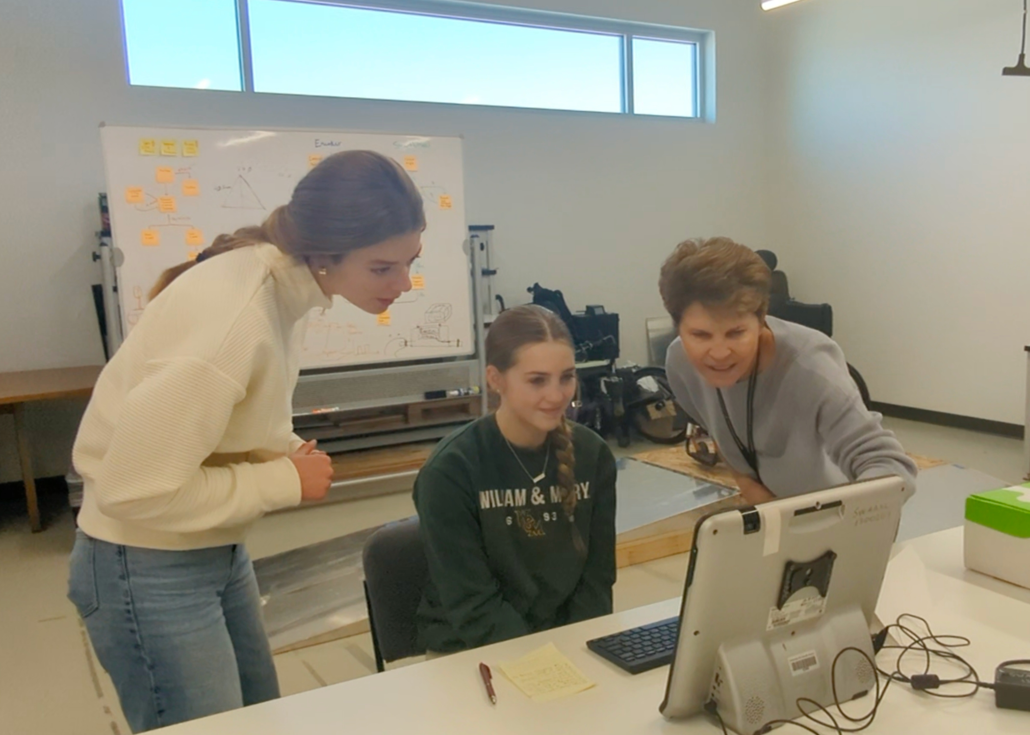 Two young women examine a monitor with a teacher