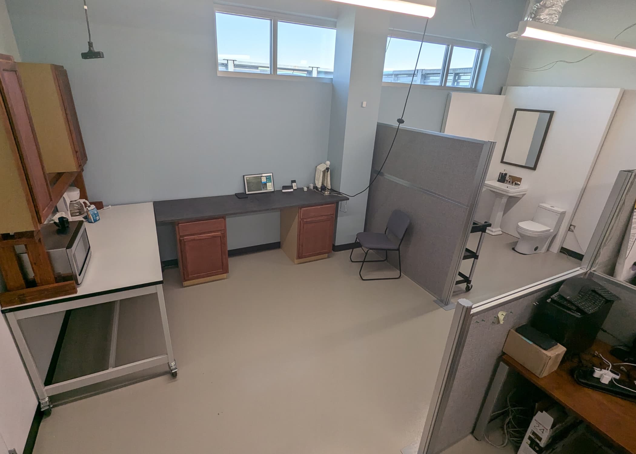 A room divided by temporary walls to form a kitchen with countertops, a bathroom with a toilet and sink, and an office with a desk