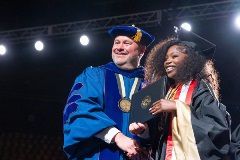 Chancellor Christensen hands a diploma cover to a smiling graduate while shaking hands on stage.
