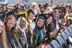 Group of students sitting in row of chairs at Commencement wearing regalia