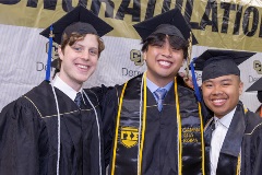 Three graduates posing together in front of large banner that reads 'Congratulations'.