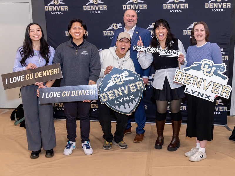 Chancellor Christensen posing with students in with props in front of wall with CU Denver Lynx logo Chancellor Christensen posing with students in with props in front of wall with CU Denver Lynx logo